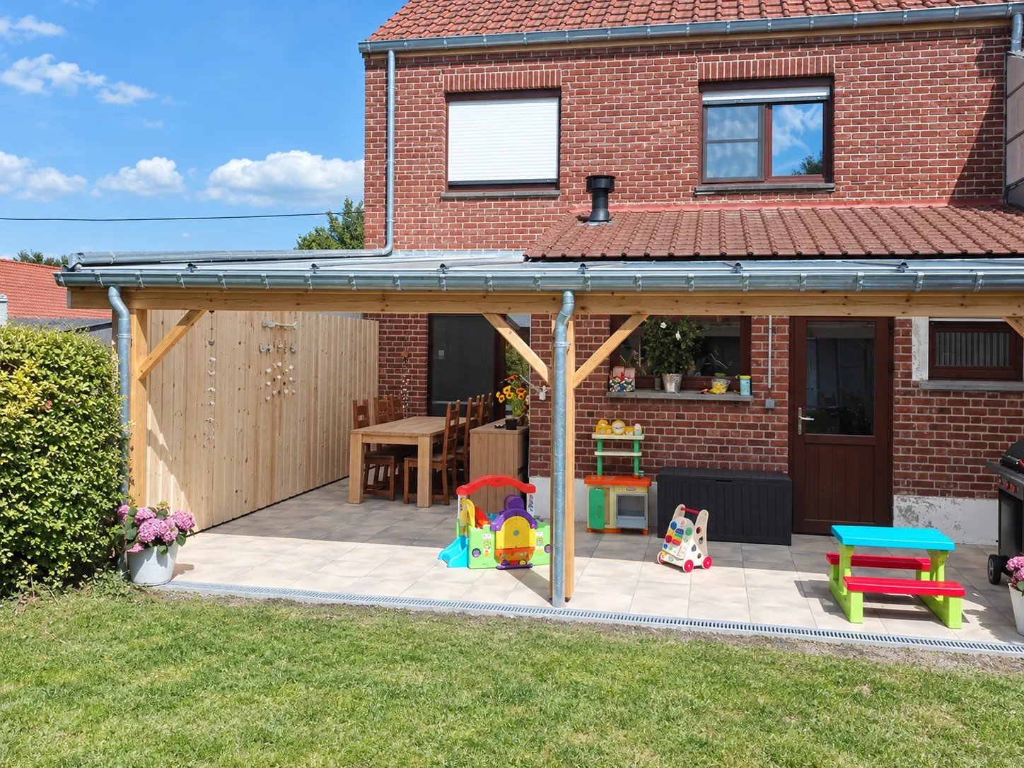 Terrasse couverte par une structure en bois devant une maison en briques