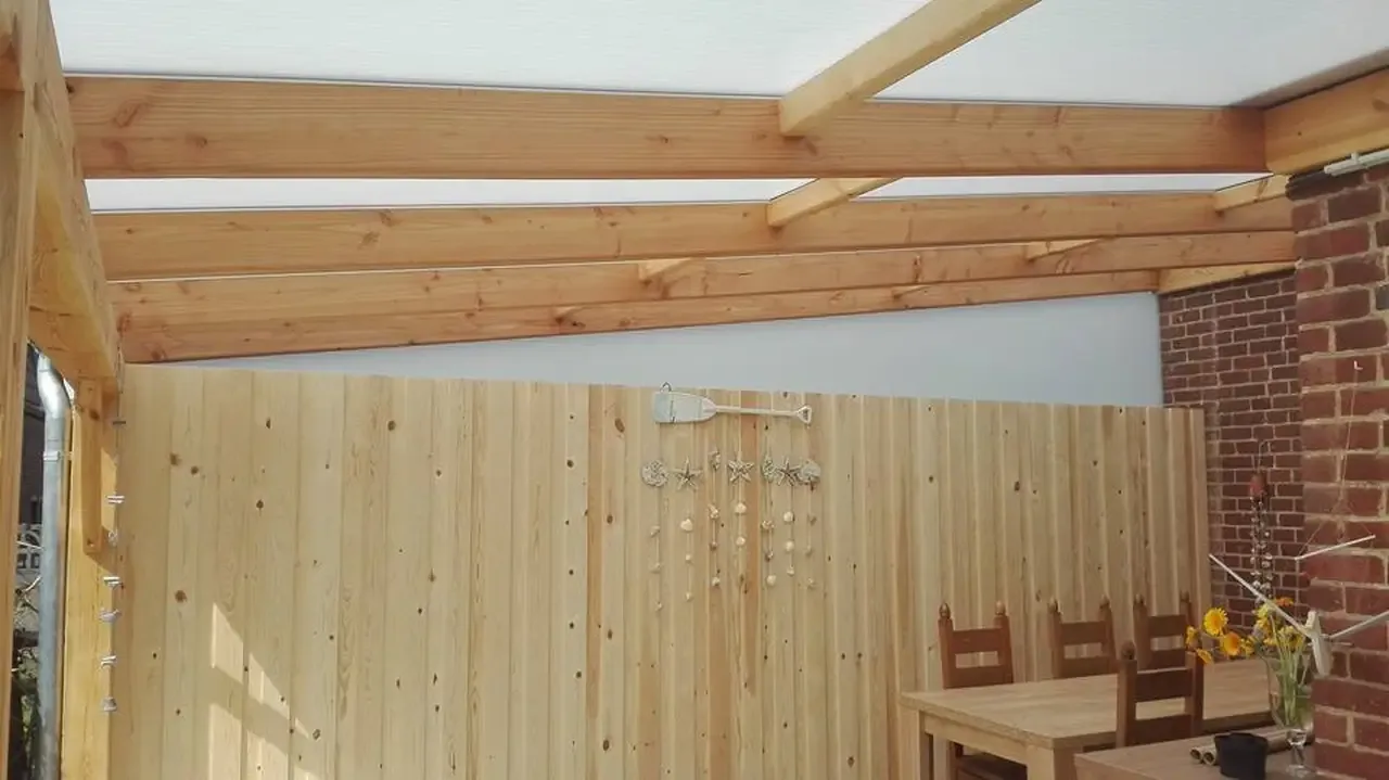 Terrasse couverte avec charpente en bois clair et bardage vertical devant un mur de briques