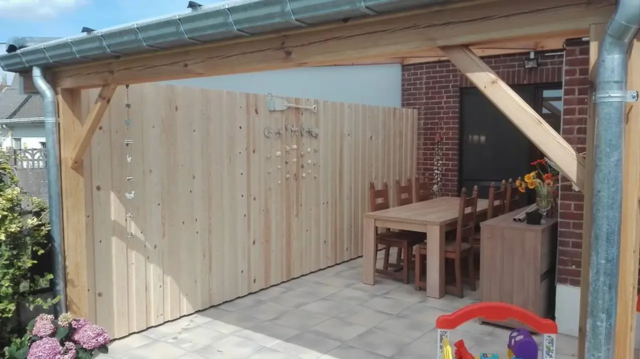 Abri en bois avec bardage en lames de bois, devant un mur en briques