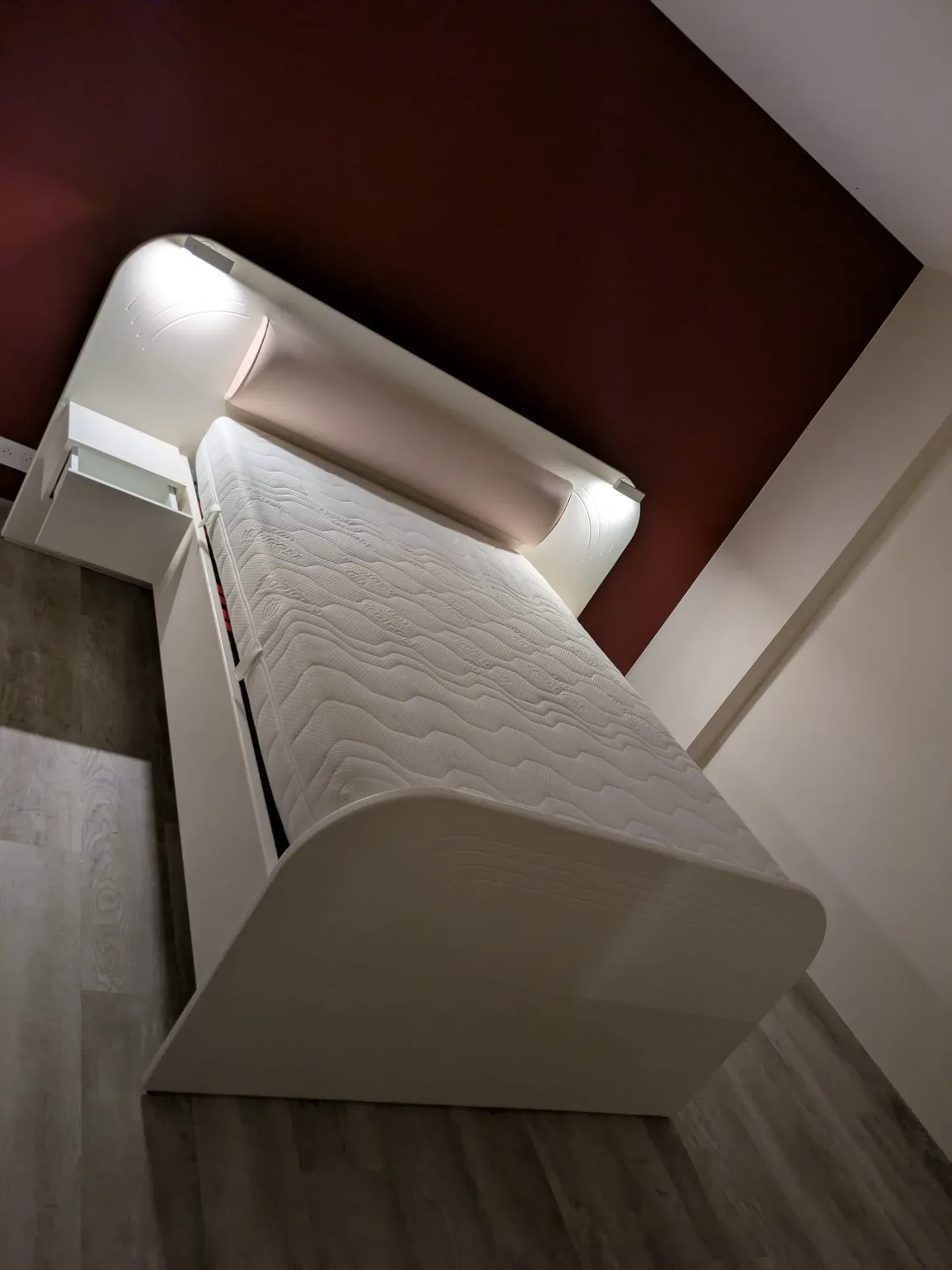 Lit sur mesure blanc cassé à tête de lit arrondie et liseuses LED intégrées, devant un mur bordeaux