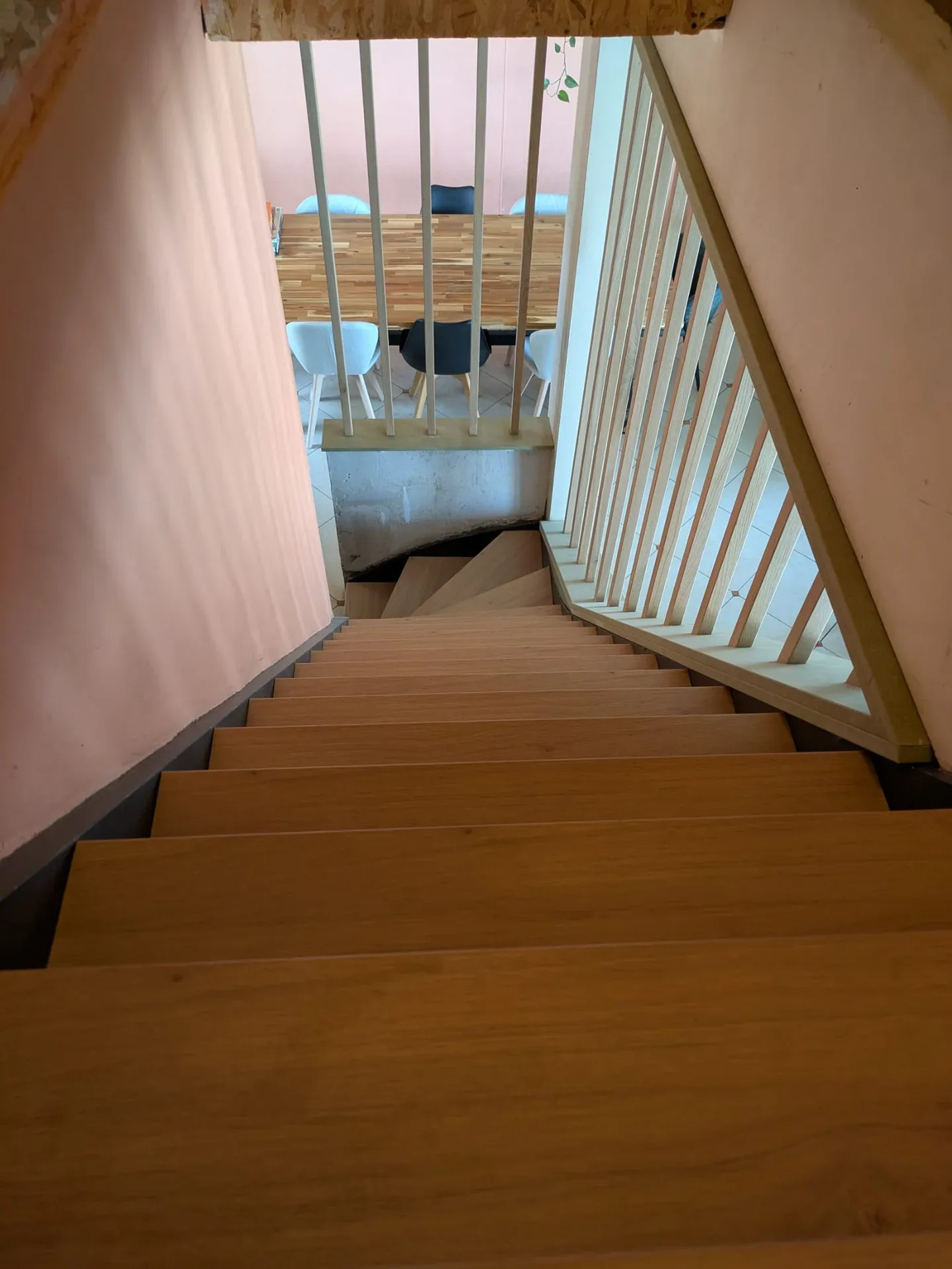 Vue plongeante sur un escalier en chêne à marches larges et balustrade à barreaux clairs