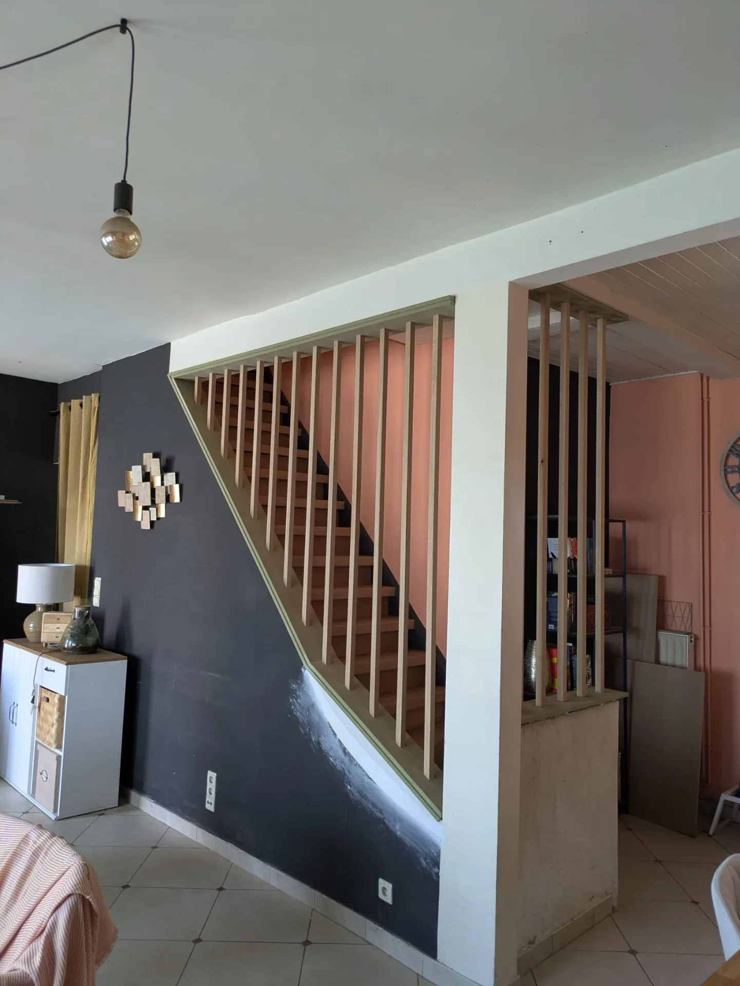 Escalier à garde-corps et cloison à lames de bois verticales dans un séjour, mur sombre et mur rose