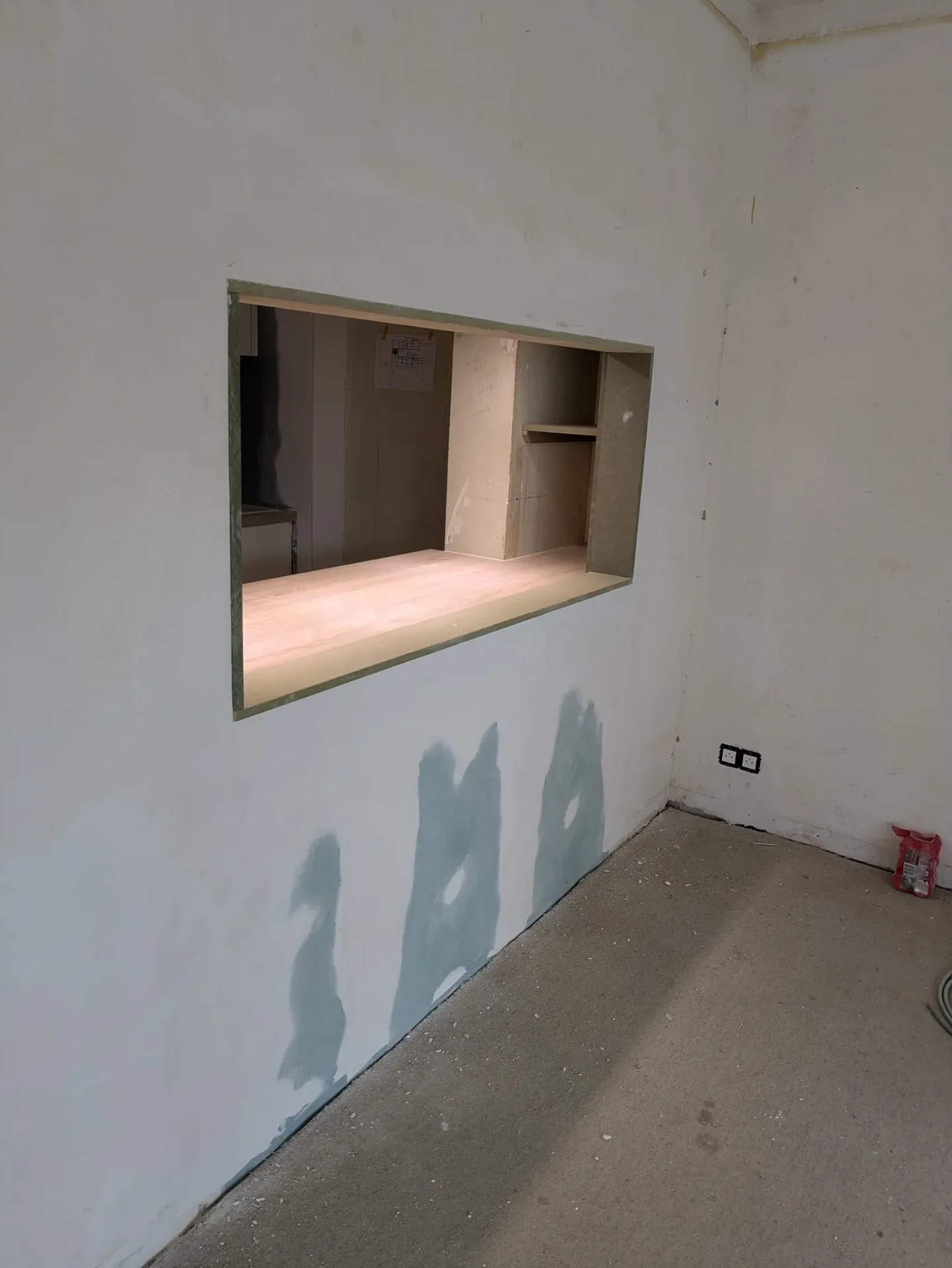 Ouverture rectangulaire percée dans un mur en cours de finition, avec habillage bois à l'intérieur, pièce brute avec sol en béton
