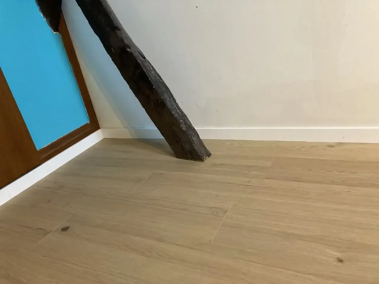 Parquet en chêne clair posé le long d’une plinthe blanche, contre une poutre ancienne sombre et un cadre de porte