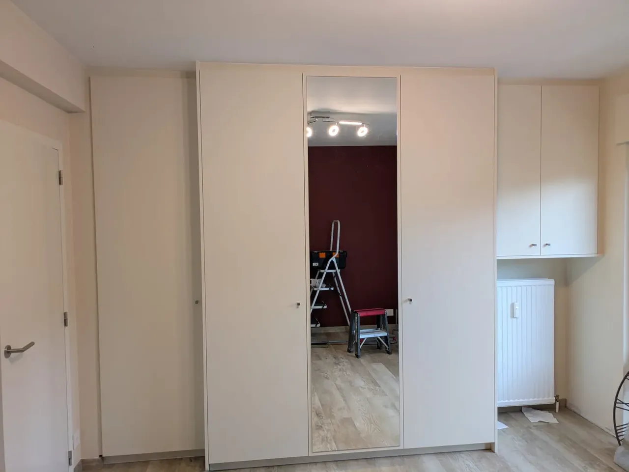 Armoire-penderie sur mesure blanc cassé avec porte miroir centrale et rangements hauts sur le côté, dans une chambre