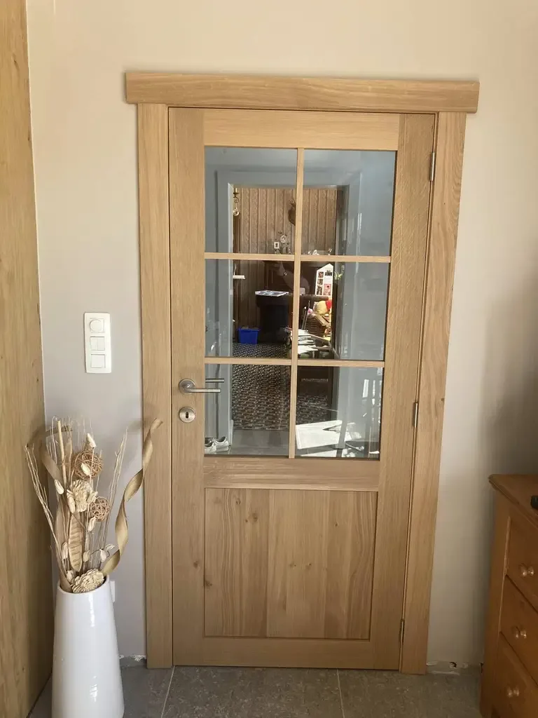 Porte intérieure en chêne clair à petits carreaux vitrés, cadre en bois et poignée métal, dans un couloir