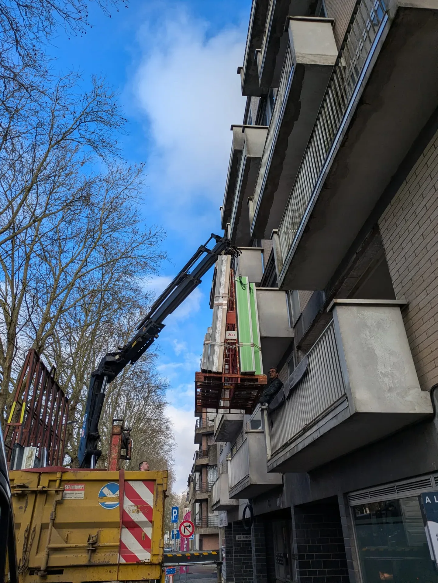 Camion-grue levant des châssis le long de la façade d'un immeuble à balcons, ciel bleu