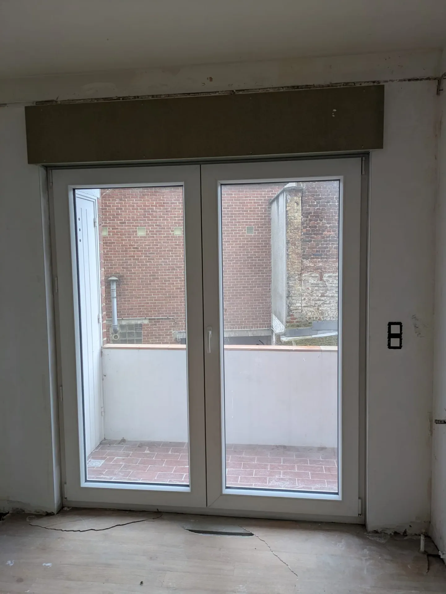 Porte-fenêtre PVC blanche à deux vantaux donnant sur un balcon carrelé, pièce en rénovation, linteau apparent