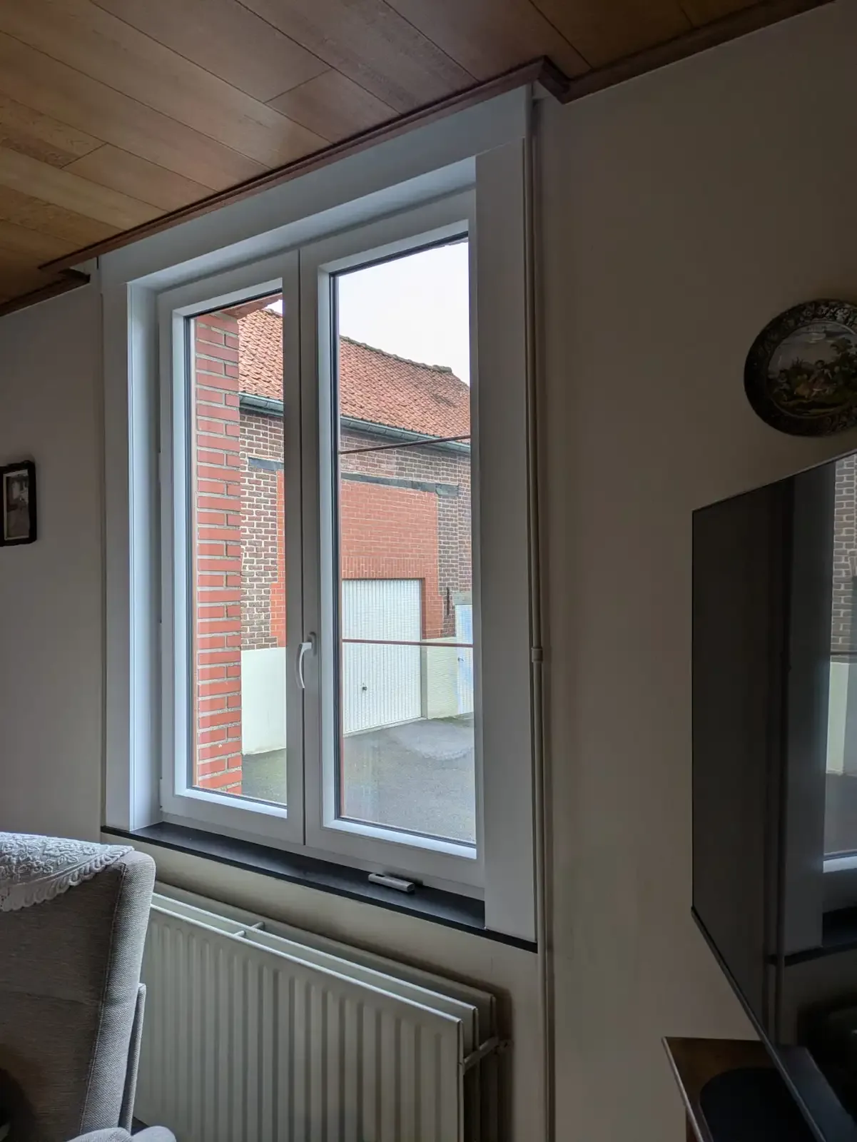 Fenêtre blanche à deux battants dans un salon, avec vue sur des maisons en briques