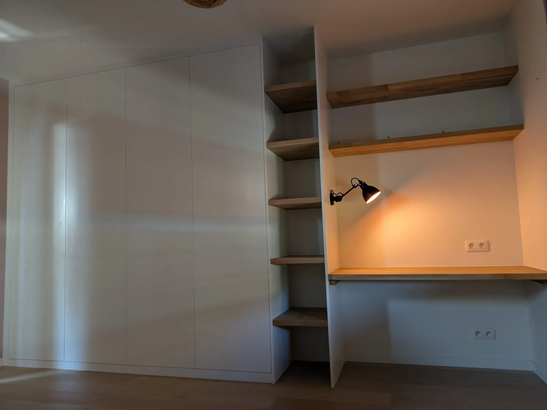 Grande armoire blanche à portes sans poignée, colonne d'étagères en chêne et coin bureau avec plan et tablettes en bois massif, lampe applique noire