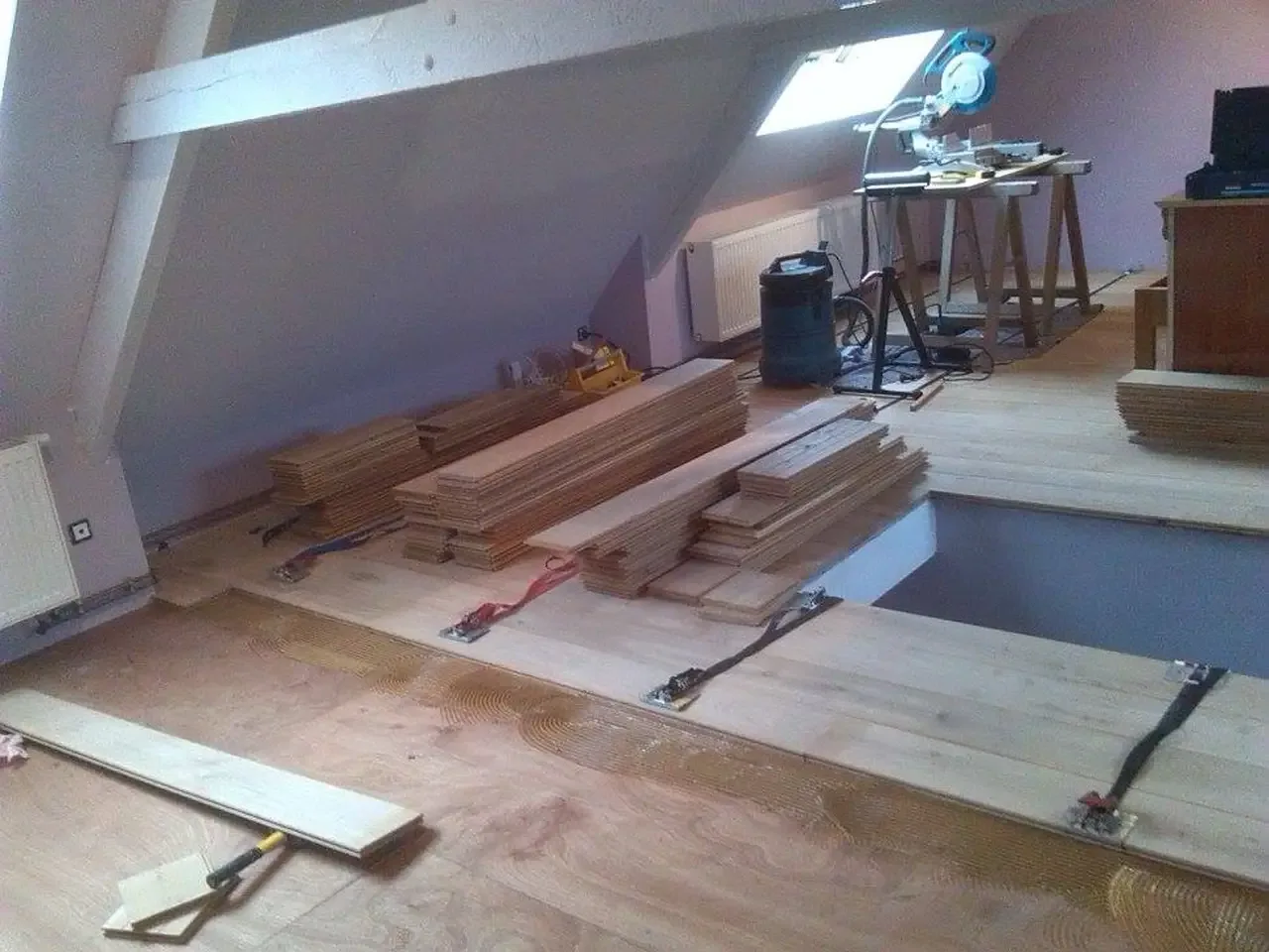 Pose d’un parquet en chêne dans une mansarde, lames empilées et sangles de serrage