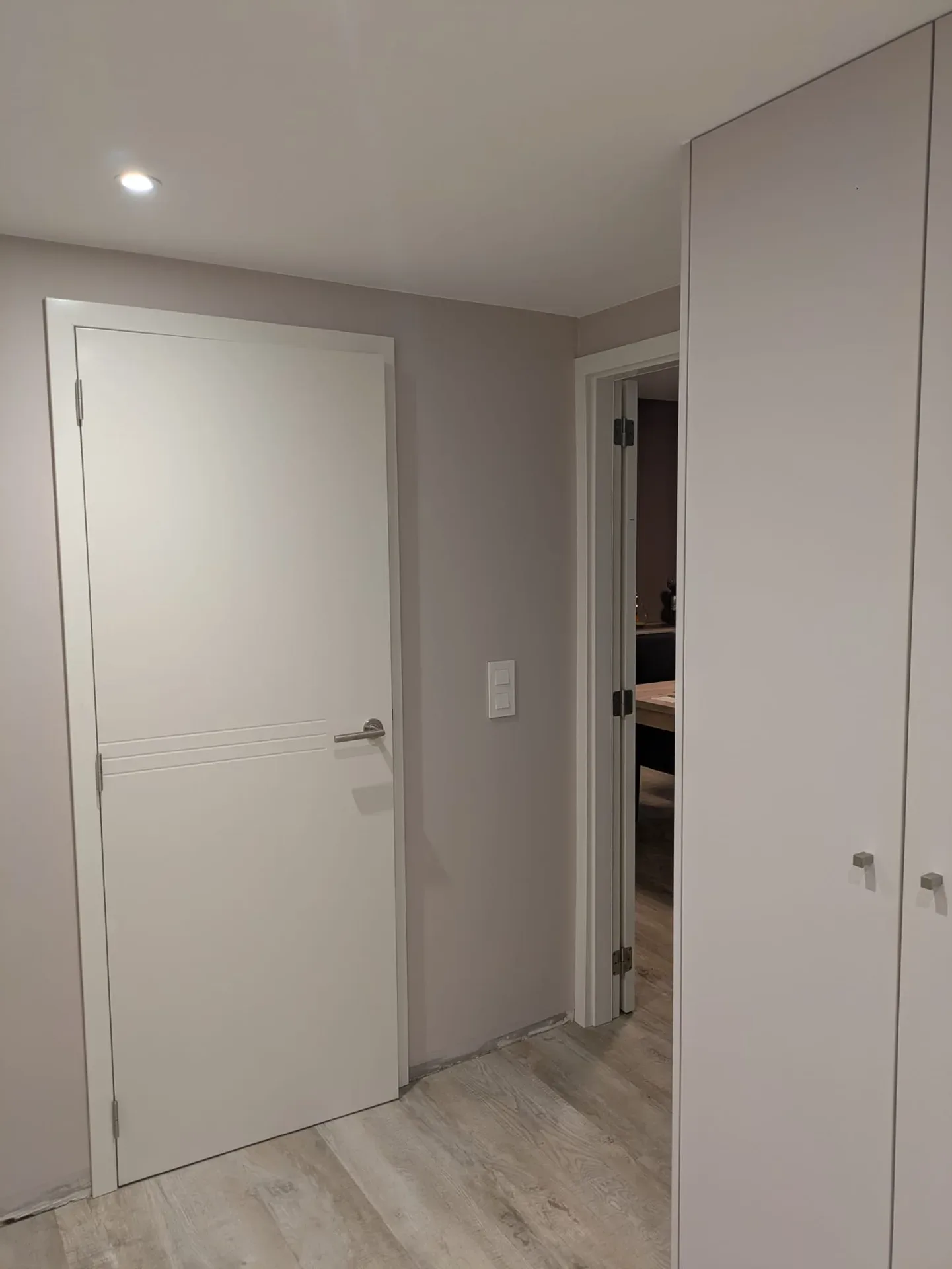 Porte intérieure blanche à rainures horizontales avec poignée inox, et grande porte d'armoire à droite, sol façon bois